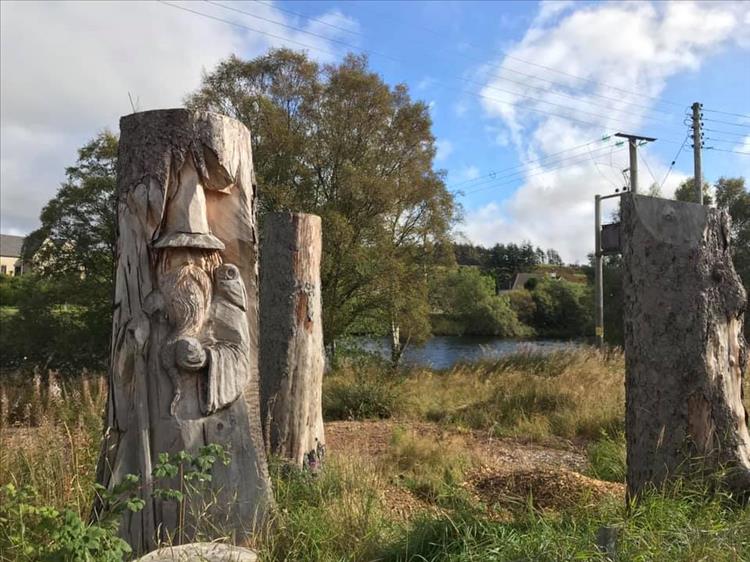 A wizard is carved into the side of a tree trunk while other trunks are mid carving