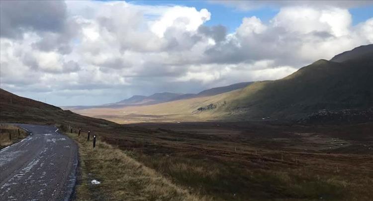 a wide broad undulating valley, a narrow lane and cloudy skies near durness