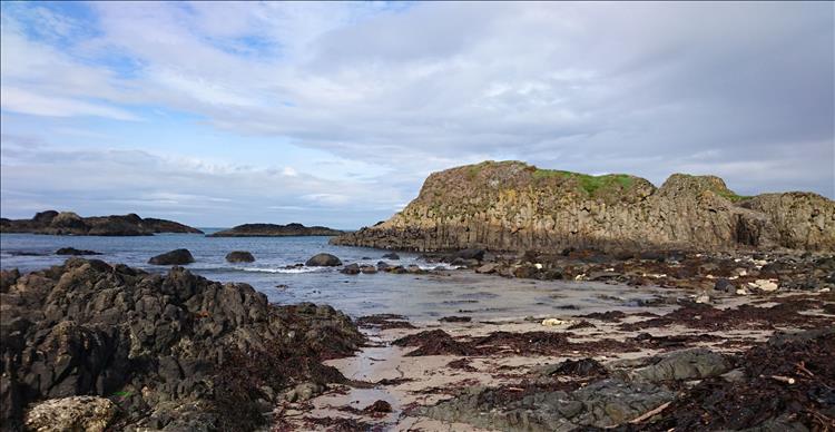 Jagged rock and sand and a craggy outcrop at Ballintoy harbour