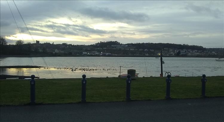 The edge of a wall overlooks the narrow strait at Bangor. We see Anglesey in the background