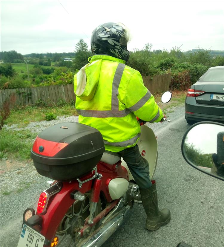 A rider on an old C90 wearing hi-viz jacket, jeans and wellington boots