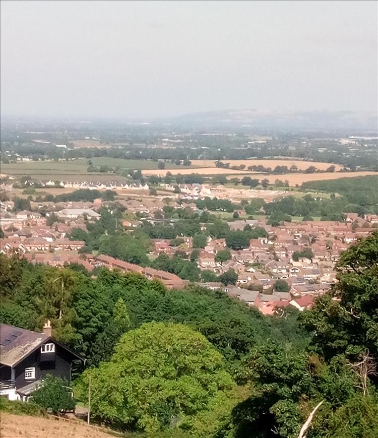 From the top of a steep hill we look down the hill and across the vast plane with a town