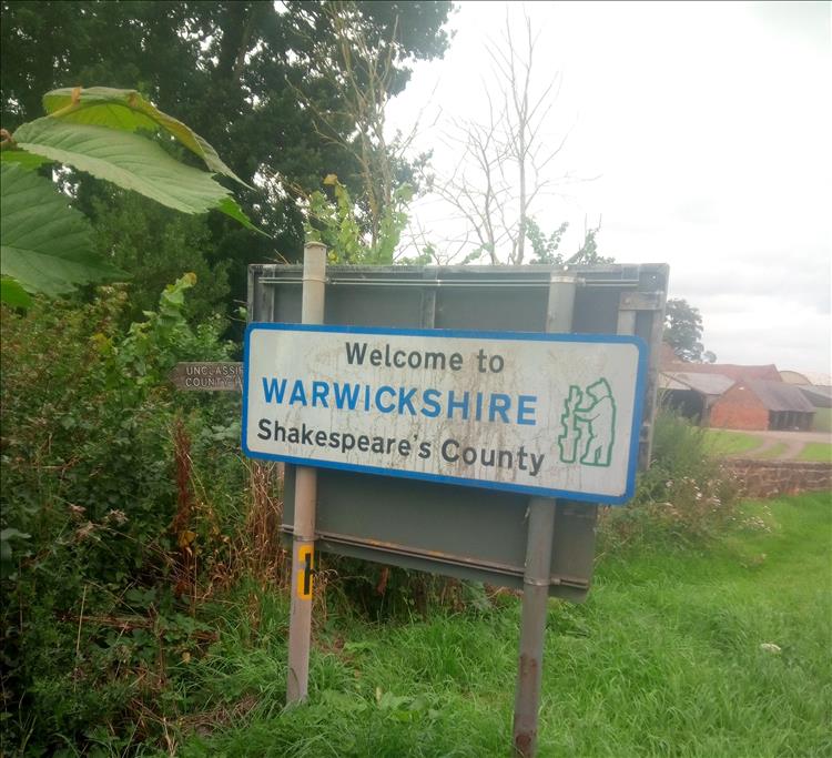 A rather dirty welcome to Warwickshire sign in the bushes by the roadside