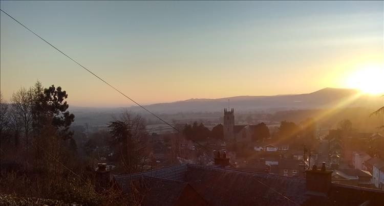 The sun pokes over the top of a distant hill with the small town of Montgomery below