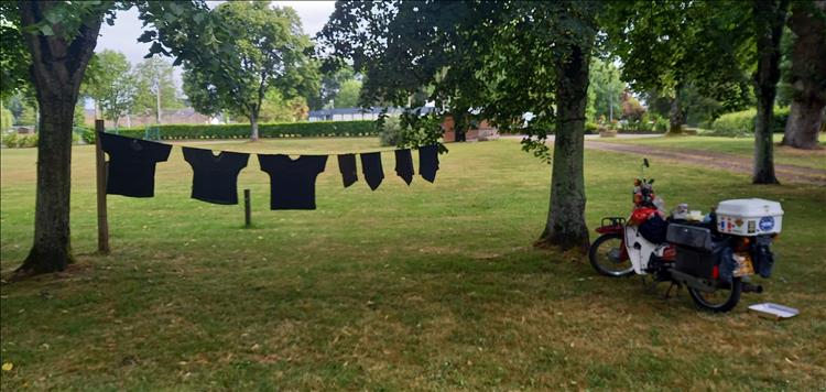 Washing on a line strung between 2 trees, by the motorcycle and the tent