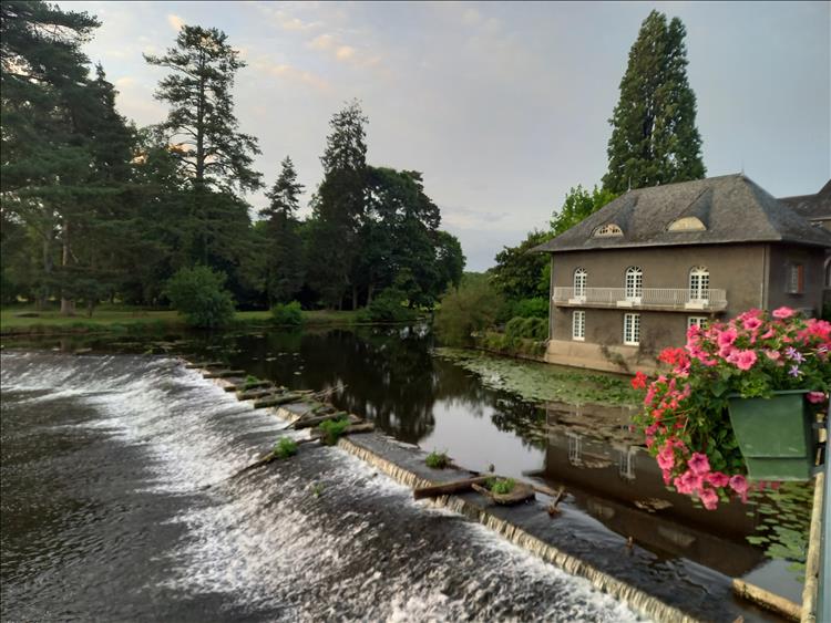 A calm river over a small weir and old pretty French buildings