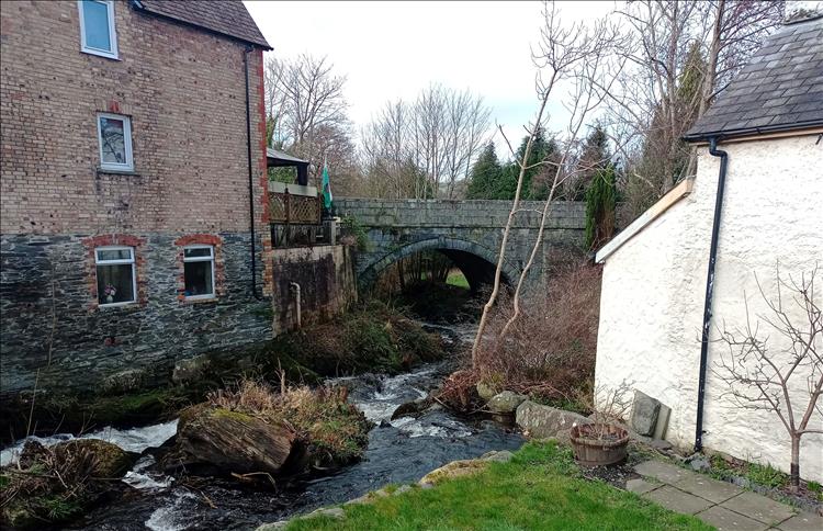 A river runs right by and between houses, a stone bridge