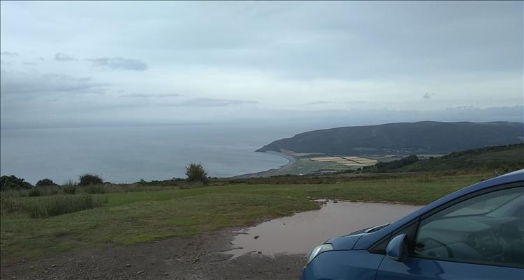 Looking down from atop a hill we see a broad beach and a flat valley at Porlock