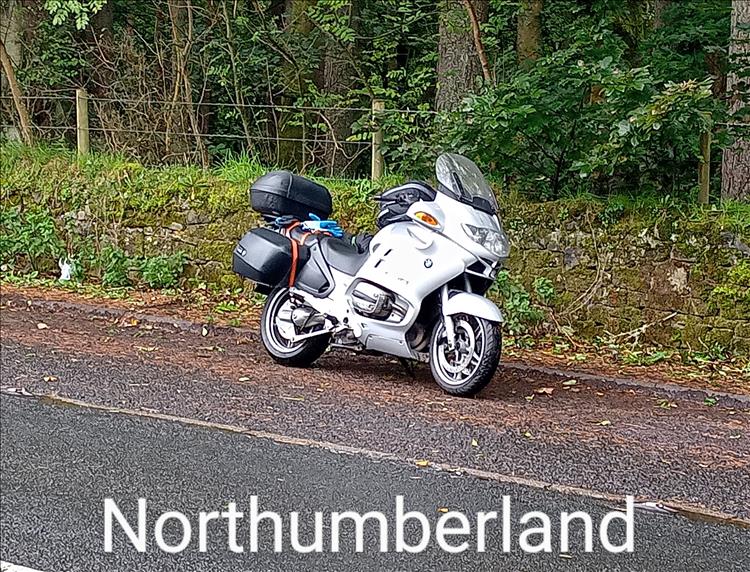 Rods big BMW by the side of a wet looking road surrounded by trees