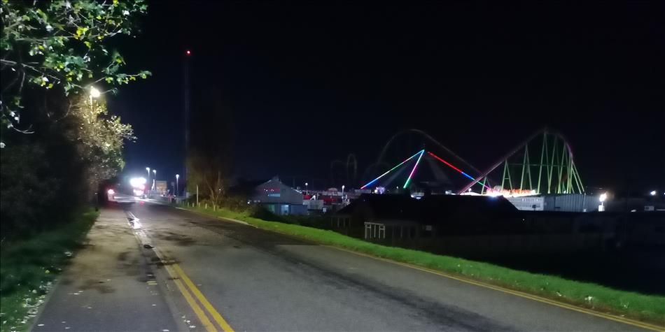 A road in the dark, in the distance colourful light light a roller coaster but no-one is around