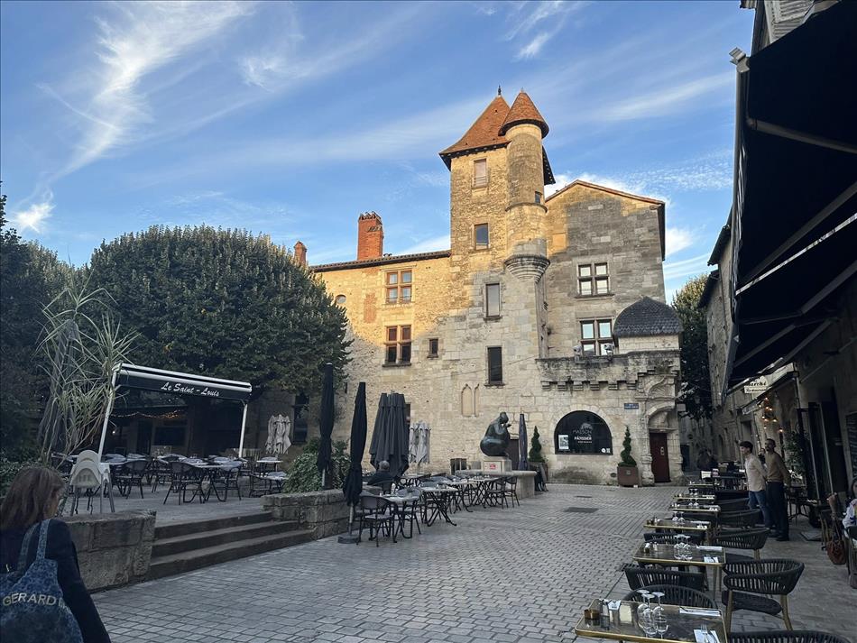 A cobbled square with a restaurant tables and trees and a building with a turret