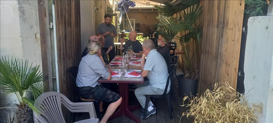 6 guests around a table, a chap is serving them