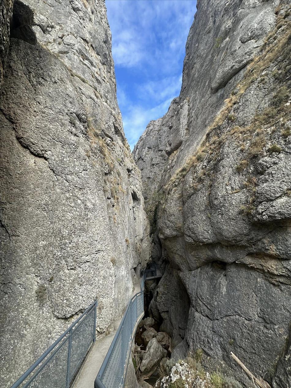 Between two vertical rocky graggy high walls a narrow steel path squeezes between