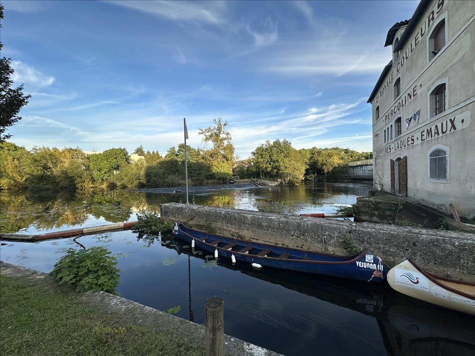Water, a weir, canoes, an old building, trees, and the river or canal and lake