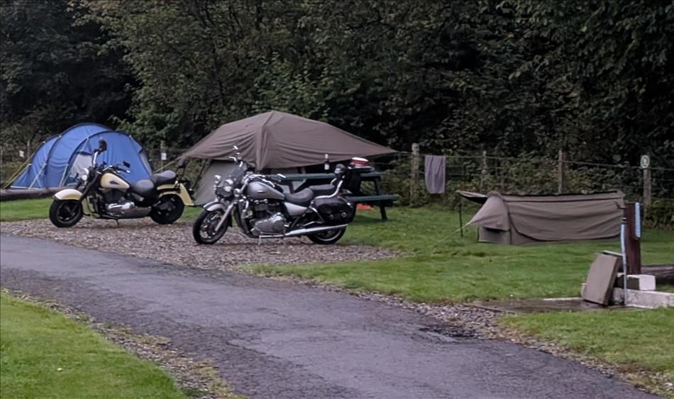 A big Kawasaki V-Twin and a big Triumph cruiser with tents and trees