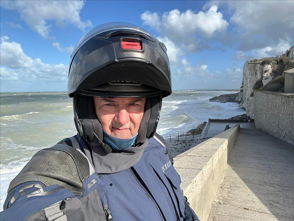 Selfie of Andy in his helmet and kit by the cliffs and sea defences with large waves