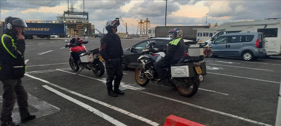 A couple for motorcycles and their riders chatting with the ferry and port in the background