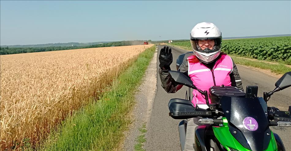Sharon waves with a smile while sat on her bike beside a wheat field in glorious sunshine in France
