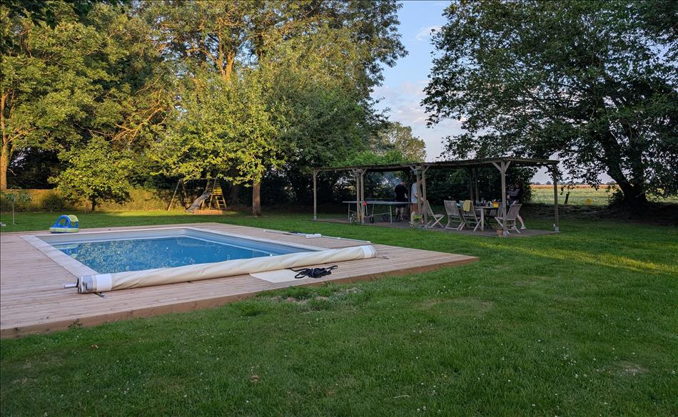 A pool maybe 15 metres in length, tables and chairs, grass and trees