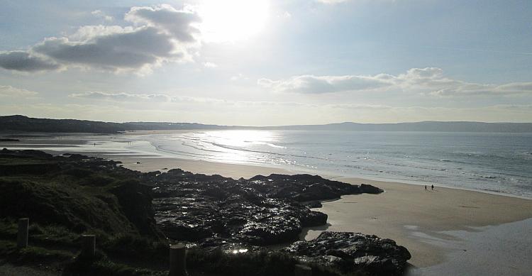 Godrevy beach in Cornwall. Bright low winter sun illuminates an almost empty vast sandy beach