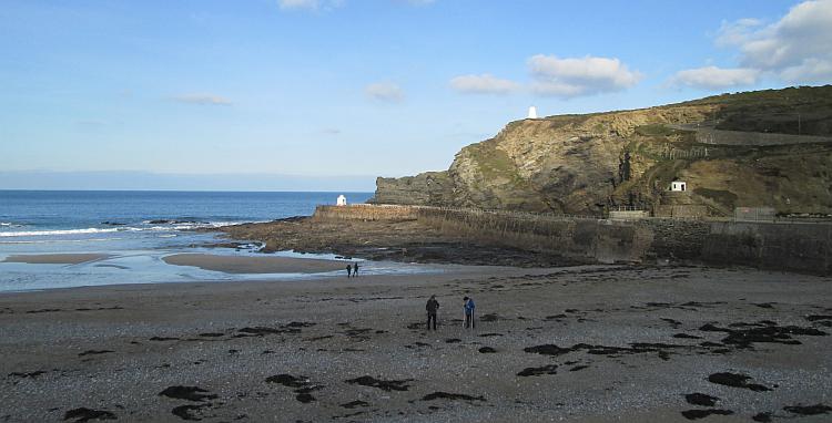 Portreath beach leading out to the sea with steep cliffs to the side and a couple of people walking along